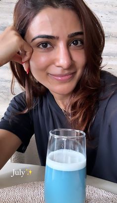 a woman sitting at a table with a glass of blue liquid in front of her