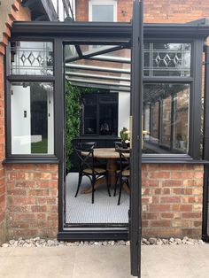 an enclosed patio with table and chairs in front of a brick wall, surrounded by glass doors