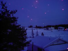 fireworks in the sky over a snow covered field at night with houses and trees on either side