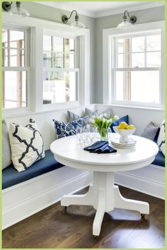 Cozy corner nook with blue cushions, white round table set with flowers, water, and lemons. Seating In Kitchen, Modern Breakfast Nook, Kitchen Booths, Decorating Rooms, Banquette Seating In Kitchen, Upholstered Banquette, Nook Table, Kitchen Breakfast Nooks