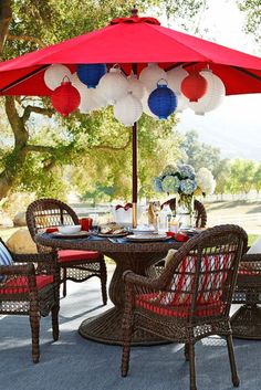 an outdoor dining set with red and white paper lanterns hanging from the umbrella over it