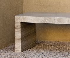 a wooden bench sitting on top of a stone floor next to a wall with no one around it