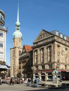 an old building with a clock tower in the background and people walking on the sidewalk