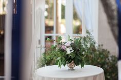 a white table topped with a vase filled with lots of flowers next to a window