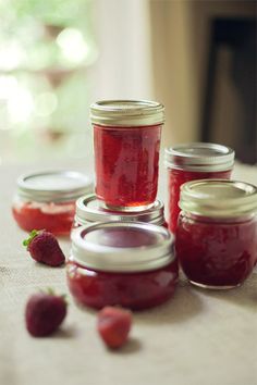 four jars filled with jam sitting on top of a table next to strawberries and another jar