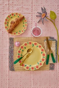 a table topped with plates and utensils on top of a pink table cloth