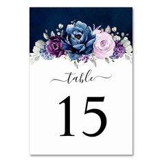 a table number card with purple flowers and greenery on the top, in front of a dark blue background