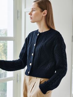 a woman standing in front of a window wearing a blue cardigan sweater and khaki pants