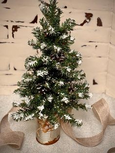 a small christmas tree in a tin can with white flowers on the top and brown ribbon around it