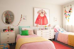 two beds in a room with colorful blankets and decorations on the wall above them are white dressers