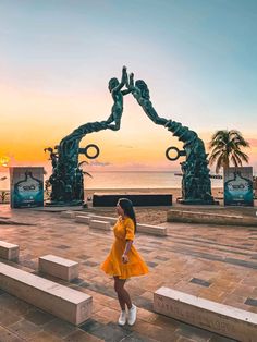 a woman standing in front of a statue on the beach at sunset with her hand up to her face