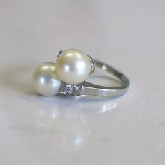 This vintage white gold ring features two large pearls at the center. Two round brilliant white diamonds are set next to them with a lovely vintage milgrain detail creating a square around each. Metal: 14K White Gold Pearls: 8.3 MM Diamonds: .10 CTW SI2 F-G Size: 5 Width: 16.5 MM @ Widest Band Width: 1.7 MM For a greater selection of jewelry please visit our website at www.BlackMarketLLC.com If you have any questions about this product or if we can help you with any of our other products please Elegant Three Stone Pearl Ring For Anniversary, Vintage White Gold Pearl Ring With Diamond Accents, Classic Platinum Pearl Ring, Classic Pearl Ring With Diamond Accents For Anniversary, Classic Three Stone Pearl Ring, Vintage White Pearl Ring With Brilliant Cut, Vintage Pearl And **** Ring, Vintage Hallmarked Pearl Ring, Vintage Hallmarked Silver Pearl Ring