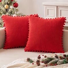 two red pillows sitting on top of a couch next to a christmas tree with pine cones