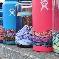 several different colored water bottles lined up on a wooden bench with mountains in the background