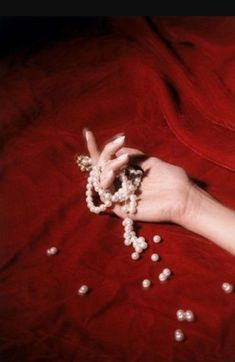 a woman's hand with pearls and beads on her wrist, resting on a red sheet