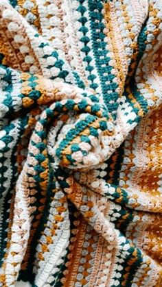 a crocheted blanket that is laying on top of a tablecloth with an orange, green and white pattern