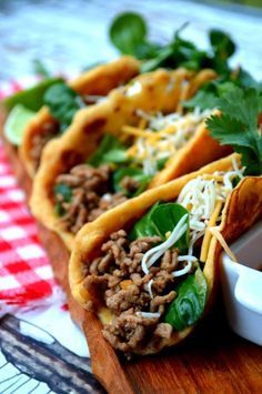 three tacos with meat, cheese and cilantro on a cutting board next to a fork