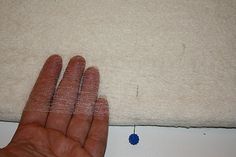 a person's hand on the edge of a piece of fabric next to a needle