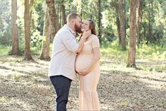 a pregnant couple standing next to each other in the woods