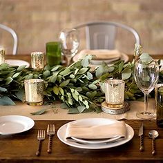 the table is set with white plates and silverware, greenery, and candles