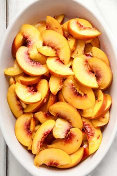 a white bowl filled with sliced peaches on top of a table