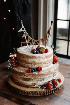 a three tiered cake with berries and bunting flags on top is sitting on a wooden table