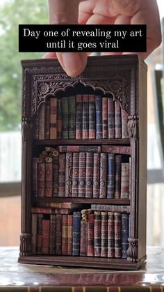 someone is holding up a miniature bookcase with books on it and the caption reads, day one of revealing my art until goes virtual