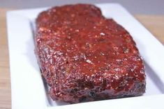 a piece of meat covered in sauce on a square white plate with a wooden table