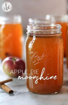 three jars filled with apple cider and cinnamons next to an apple on the table