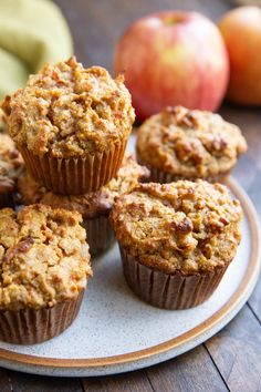 several muffins on a plate with apples in the background