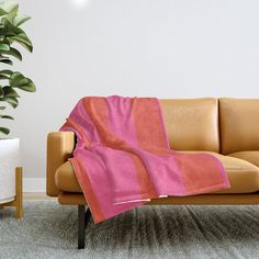 a couch with a pink and orange blanket on it next to a potted plant