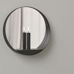 two candles are lit in front of a round mirror on the wall next to a candle holder