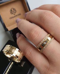 a woman's hand with two gold rings in front of an open ring box