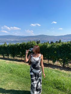 a woman standing on top of a lush green field drinking out of a water bottle