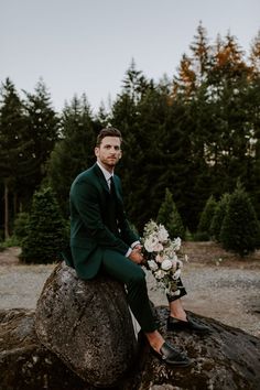 a man in a suit and tie sitting on top of a rock holding a bouquet