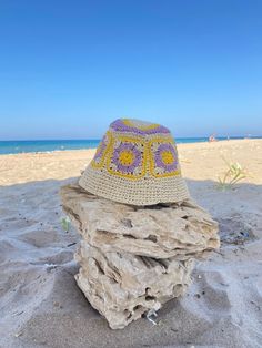 a crocheted hat sitting on top of a rock in the sand at the beach