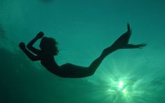 a woman is swimming in the water with her arms up and legs spread out as she dives