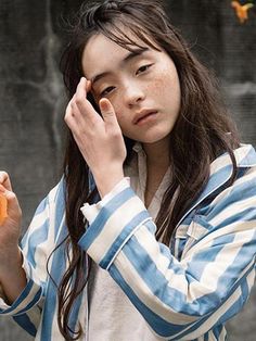 a young woman holding an orange in her right hand and looking at the camera with one hand