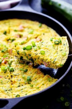 an omelet in a pan with a spatula and green onions on the side