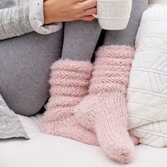 a woman sitting on a bed with her legs crossed and holding a coffee cup in her hand