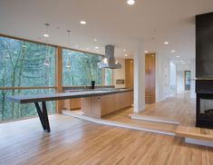 an empty kitchen and living room with large windows overlooking the trees outside, is shown in this image