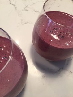 two glasses filled with smoothie sitting on top of a white marble countertop next to each other