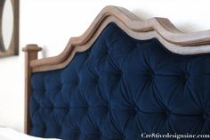 an upholstered headboard on a bed with white sheets and blue velvets