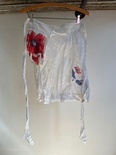 a white shirt with red flowers on it hanging from a wooden hanger next to a wall