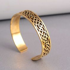 a gold bracelet with an intricate design on the front and back, sitting on a table