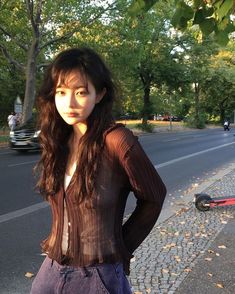 a young woman standing on the side of a road next to a tree filled street