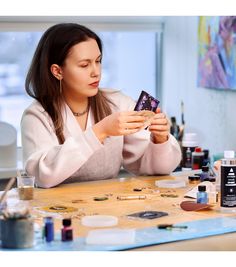 a woman is sitting at a table with her hands on a piece of art work