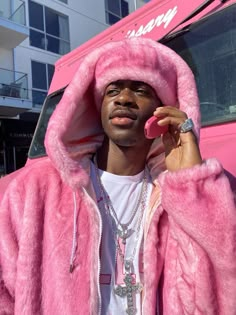 a man in a pink fur coat talking on a cell phone while standing next to a pink truck