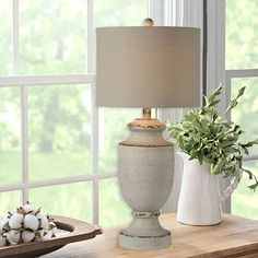 a lamp on a table next to a vase with flowers and cotton in front of a window