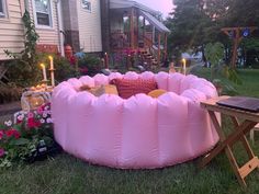 a large pink inflatable pool sitting on top of a lush green field next to a house